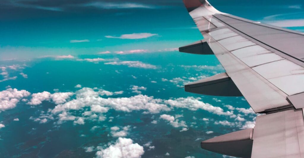 Aerial view of airplane wing over fluffy clouds with a deep turquoise sky.