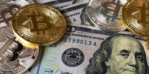 A close-up photo depicting Bitcoin coins on top of US dollar bills, symbolizing finance and cryptocurrency.