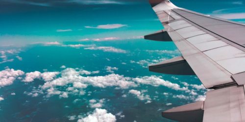 Aerial view of airplane wing over fluffy clouds with a deep turquoise sky.